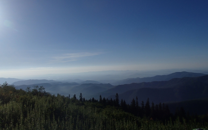 Under a blue sky, there is a mountainous landscape and green trees.